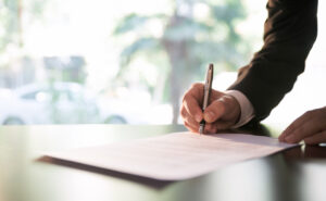 Person in a suit signing a legal document at a desk, emphasizing the role of defendants in personal injury cases.